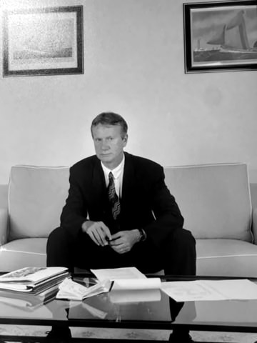 Norbert Miconnet assis dans un canapé, dossiers ouverts sur une table basse, photographie en noir et blanc